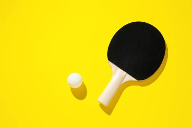 Sarı arka planda pinpon raketi ve top, üst manzara. Metin için boşluk