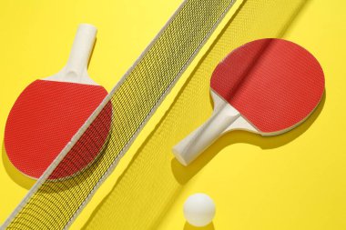 Sarı arka planda pinpon raketleri, top ve ağ.
