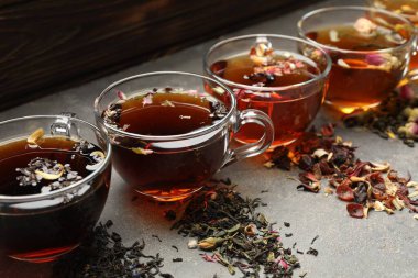 Cam fincanlarda aromatik bitki çayı ve gri masada kuru yapraklar, yakın plan.