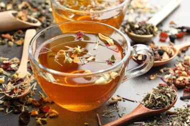 Aromatik bitki çayı ve kuru yapraklar gri masada, yakın plan.