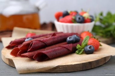 Lezzetli meyve dürümleri, çilekler, yaban mersinleri ve nane şekeri gri ahşap masada, yakın plan.