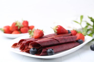 Lezzetli meyve dürümleri, çilekler ve yaban mersinleri beyaz masada, yakın plan. Metin için boşluk