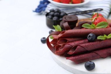 Lezzetli meyve dürümleri, çilekler, yaban mersini ve nane şekeri beyaz fayanslı masada, yakın plan. Metin için boşluk