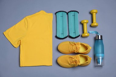 Spor kıyafetleri, bilek ağırlıkları, su şişesi ve gri arka planda dambıllar, düz yatış.