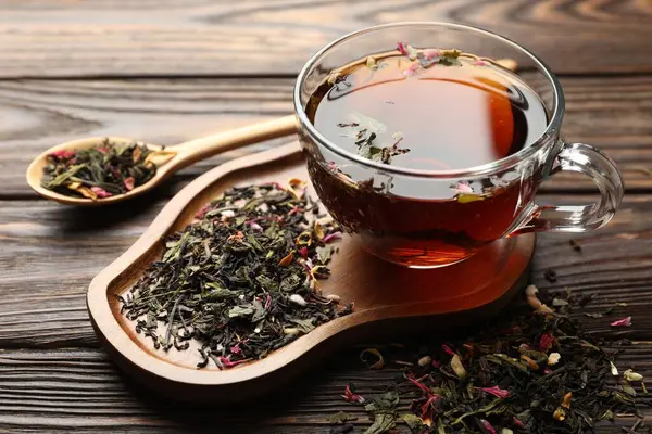 Cam bardakta Aromatik bitki çayı ve ahşap masada kuru yapraklar, yakın plan.