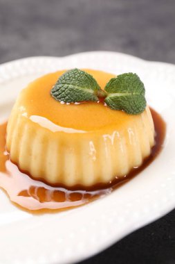 Karamel soslu lezzetli puding ve gri masada nane şekeri, yakın plan.