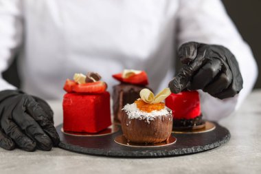 Mutfaktaki açık gri masada lezzetli bir tatlıyı dekore eden şekerci, yakın plan.