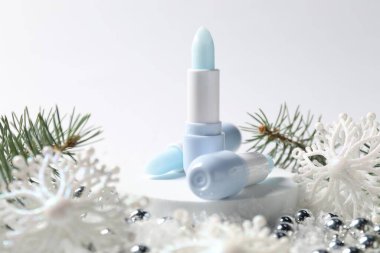 Nemlendirici dudak kremleri, Noel dekorasyonu ve beyaz arka planda suni kar üzerindeki köknar ağacı dalları, yakın plan. Kış bakımı