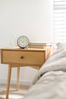 İçinde kitaplar, çalar saat ve yatağın yanında bir bardak su olan komodin.