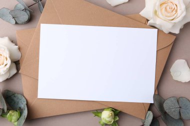 Boş tebrik kartı, kağıt zarflar, gül çiçekleri ve bej arka planda okaliptüs dalları, düz uzanma