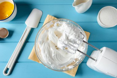 Açık mavi ahşap masada çırpılmış krema ve çırpılmış çırpılmış çırpılmış çırpılmış çırpılmış çırpıcı, düz uzanmış.