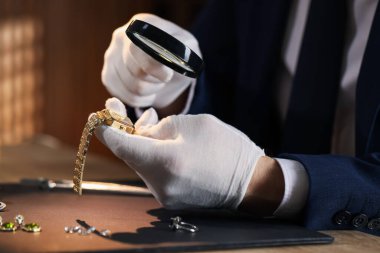 Büyüteci olan bir eksper. Masadaki lüks kol saatini değerlendiriyor. Yakın plan.