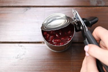 Kadın konserve açacağıyla konserve açıyor. Ahşap masada, yakın plan.