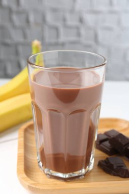 Bardakta çikolatalı süt, beyaz ahşap masada muzlar, yakın plan.