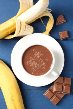 Lezzetli çikolatalı süt, parçalar ve muzlar mavi ahşap masada, düz uzanmış