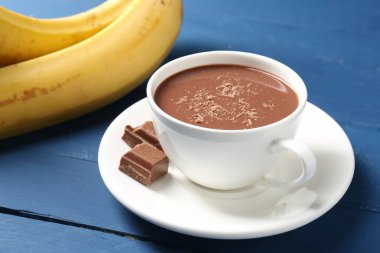 Lezzetli çikolatalı süt, parçalar ve muzlar mavi ahşap masada, yakın plan