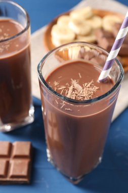 Lezzetli çikolatalı süt bardaklarda, parçalar ve muz mavi ahşap masada, yakın plan