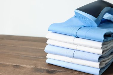 Dik vapur ve beyaz duvarın yanındaki ahşap masada katlanmış gömlekler, yakın plan. Metin için boşluk