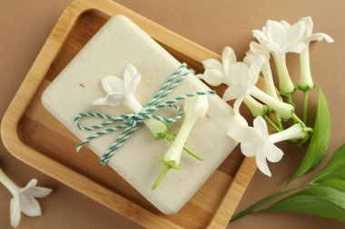 Açık kahverengi arka planda sabun ve yasemin çiçekleri, düz uzanmış.