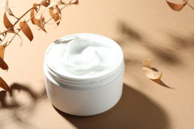 Bej arka planda bir kavanoz vücut kremi ve kuru dallar, yakın plan.