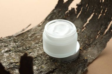 Bej arka planda vücut kremi ve ağaç kabuğu kavanozu, yakın plan.