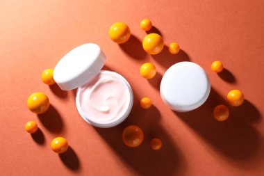 Kavanozlar dolusu nemlendirici vücut kremi ve turuncu arka planda toplar.