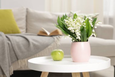 Bir buket güzel vadi zambağı ve kahve masasının üstünde elma.