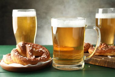 Lezzetli krakerler ve yeşil ahşap masada bira bardakları Gri arka planda, yakın plan