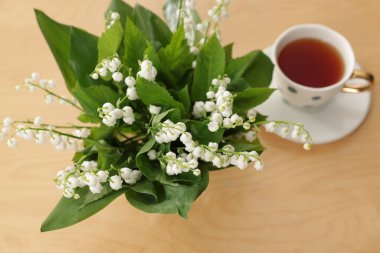 Vadideki güzel zambak buketi ve ahşap masada bir fincan çay, yakın plan.