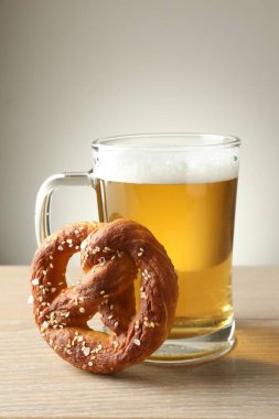 Lezzetli kraker ve bir bardak bira ahşap masada, gri arka planda, yakın planda.