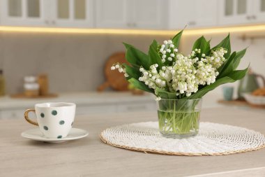 Vadideki güzel zambak buketi ve mutfaktaki ahşap masada duran kupa.