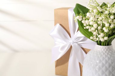 Vadi çiçeklerinin güzel zambakları ve beyaz masada hediye, yakın plan. Metin için boşluk