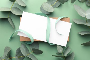 Açık yeşil zemin üzerinde boş kart, kurdele ve okaliptüs dalları, düz yatıyordu