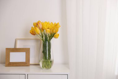 Beyaz duvarın yanındaki masada bir buket güzel lale ve resim çerçevesi. Metin için boşluk