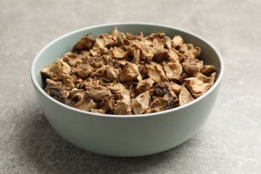 Kase içindeki kuru hindiba kökleri gri desenli masada, yakın plan.