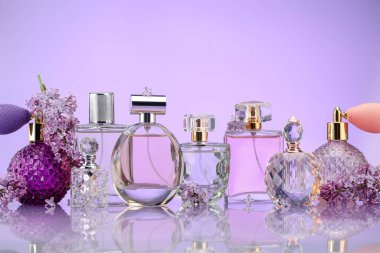 Ayna yüzeyinde mor arka planda parfüm şişeleri ve leylak çiçekleri