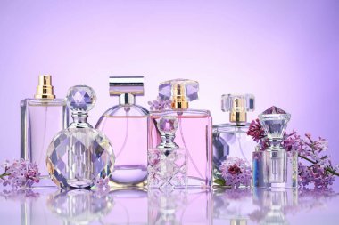 Ayna yüzeyinde mor arkaplana karşı parfüm şişeleri ve leylak çiçekleri