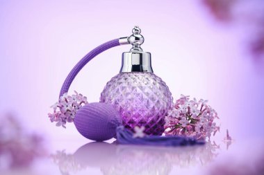 Bir şişe parfüm ve ayna yüzeyinde eflatun rengine karşı leylak çiçekleri, seçici odak