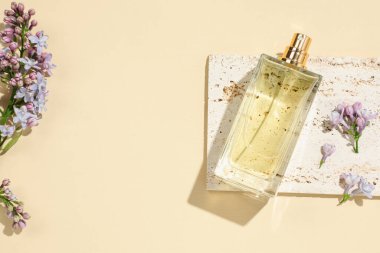 Bir şişe parfüm ve soluk sarı arka planda güzel leylak çiçekleri. Metin için boşluk
