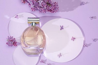 Bir şişe parfüm ve açık mor arka planda güzel leylak çiçekleri.