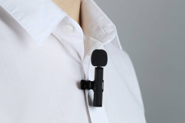 Gri arka planda gömleğine mikrofon takmış bir adam.