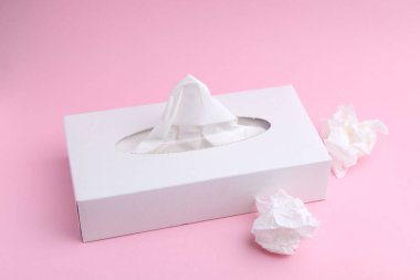Kağıt mendilli kutu ve pembe arka planda buruşmuş mendil.
