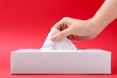 Kırmızı arka planda mendili kutusundan çıkaran kadın, yakın plan.