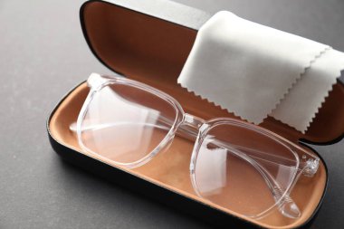 Gri arka planda şık gözlüklü ve temizlik bezli çanta, yakın plan.