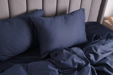 Evinde koyu mavi ipek çarşaflar olan bir yatak.