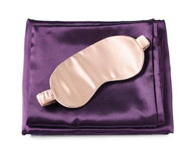 Beyaz arka planda ipek çarşaflar ve uyku maskesi, üst manzara.