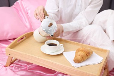 Kadın Moka çaydanlığından bardağa kahve dolduruyor pembe ipek çarşaflarla, yakın plan.