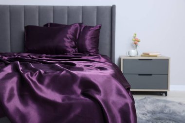 Lüks ipek çarşaflar yatağın üzerinde ve komodinin üzerinde.