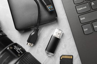 Flaş bellek, SD hafıza kartı, harici hard disk, dizüstü bilgisayar ve kamera lensleri gri desenli tabloda, düz konum