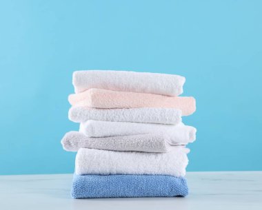 Açık mavi arkaplana karşı beyaz mermer masaya temiz havlu yığını